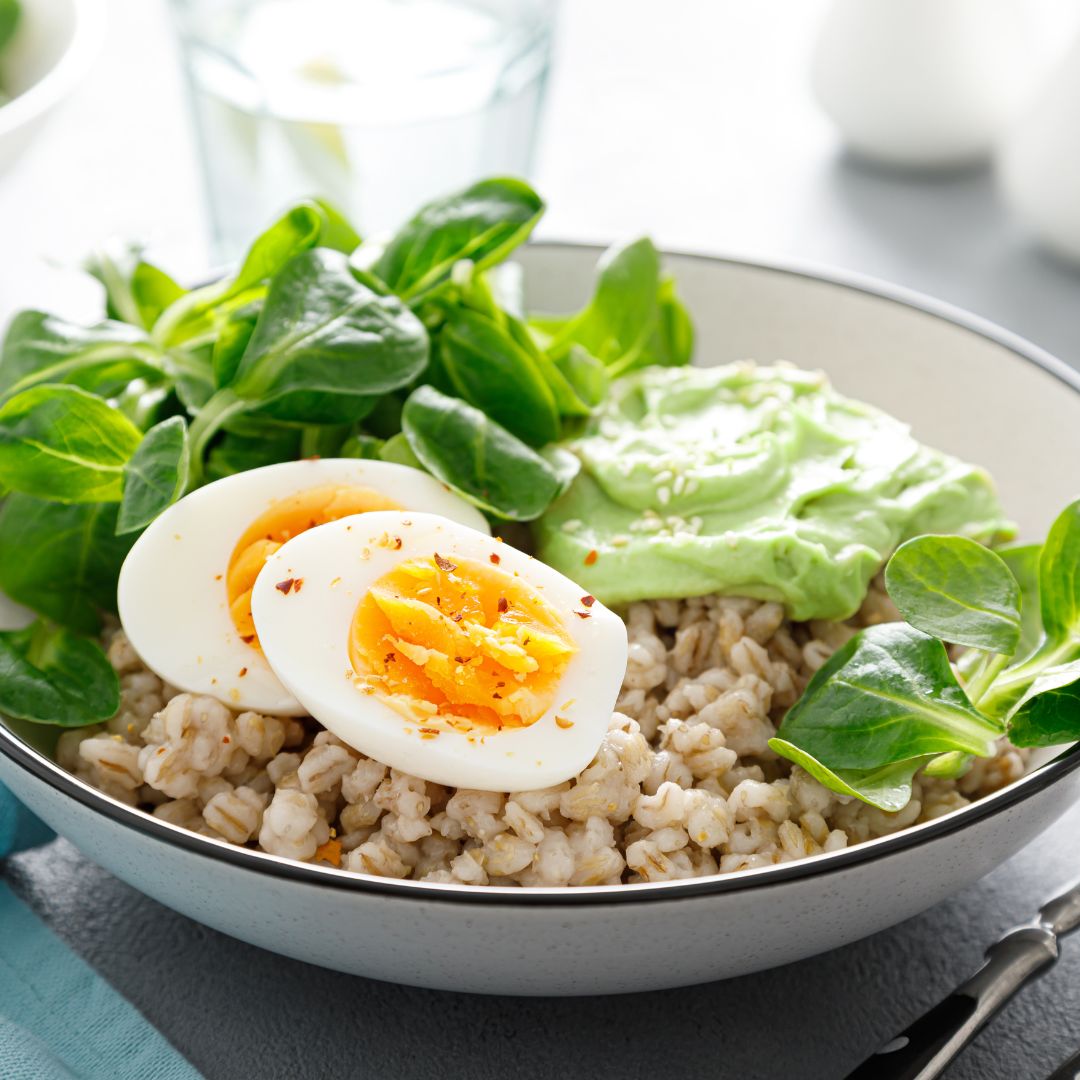 Bowl of pearl barley risotto with leeks, shredded Brussels sprouts and cabbage, topped with halved soft-boiled eggs, toasted hazelnuts and parsley